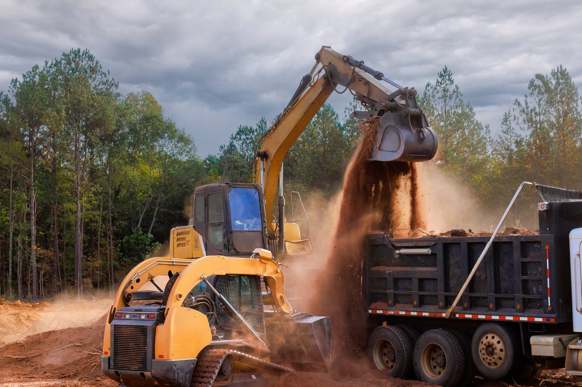 Heavy machinery transferring soil to a dump truck during land levelling