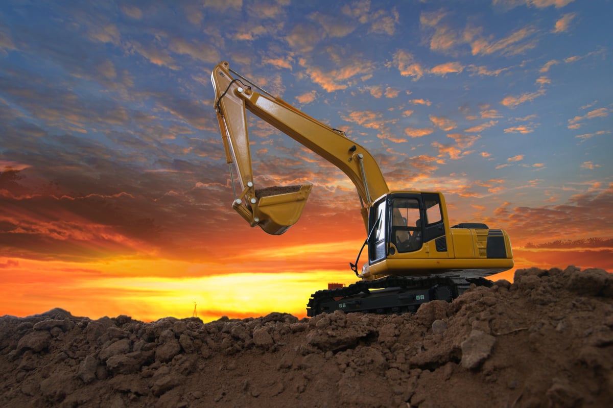 Crawler excavators digging soil at a construction site on a sunset